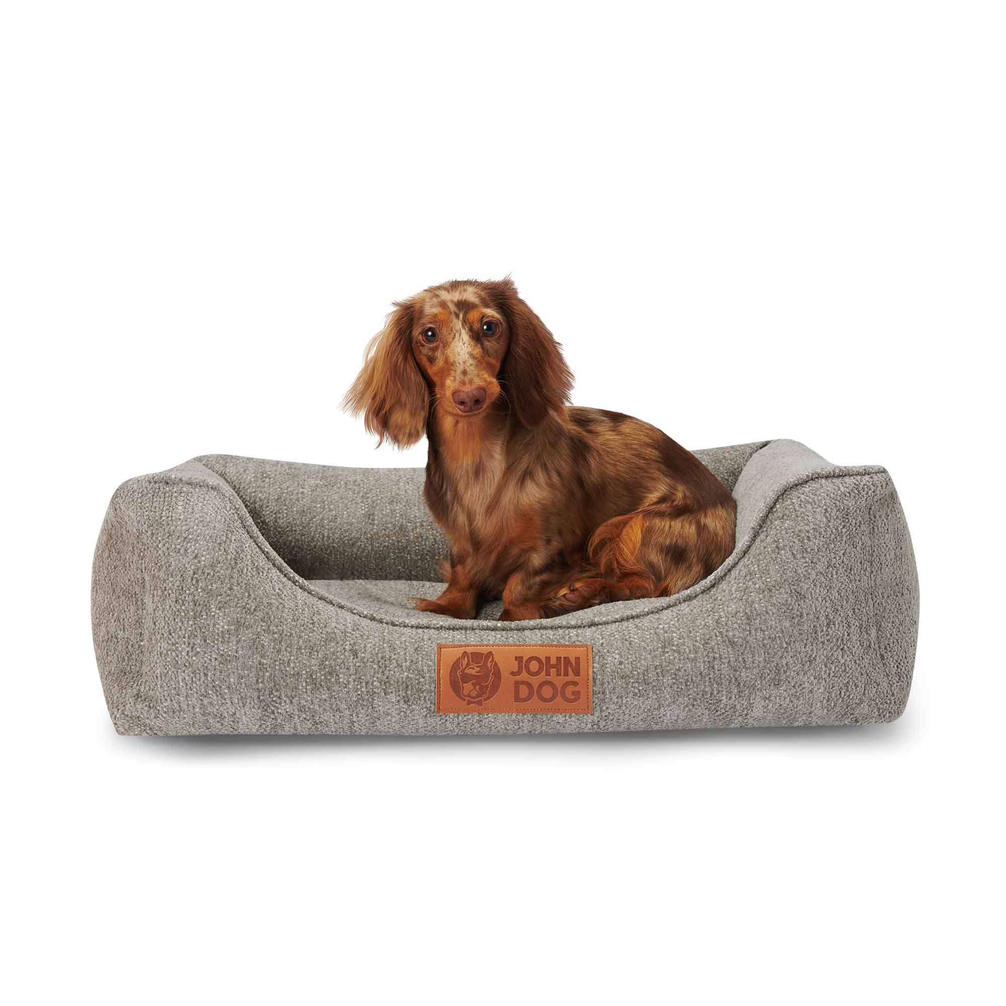 Ein niedlicher Dackel sitzt auf dem grauen Hundebett HARMONY von John Dog, das sich perfekt in seine Silhouette einfügt. Das Bett bietet Komfort und hervorragenden Halt für dein Haustier und sieht dabei auch noch elegant aus.