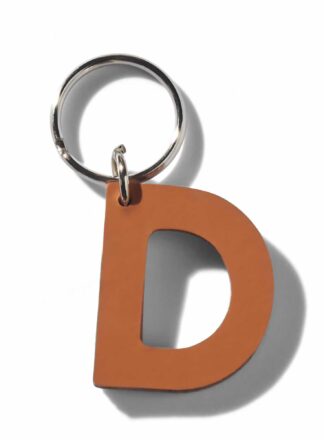 Brauner Lederschlüsselanhänger für Leine, Geschirr oder Halsband in Form des Buchstabens "D" aus der MANIFEST Kollektion von John Dog. Der Schlüsselanhänger kann als Initiale für den Namen deines Hundes verwendet werden.